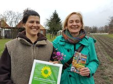 Man sieht zwei lachende Frauen im Herbst, der Hintergrund ist kahl, das Feld dahinter abgeerntet. Nur vereinzelt blühen noch lila die Kartäusernelken. Links mit dunklen Haaren ist Nina Keller, die Botanikerin und Gründerin von "Die Wildblume". Rechts mit der Urkunde in der Hand ist die Landesvorsitzende von Bündnis 90/Die Grünen in Brandenburg, Petra Budke. Um sie herum sind viele Journalisten, die man aber auf dem Bild nicht sehen kann.