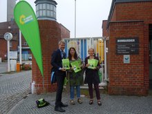 drei Grüne AKtive stehen vor dem Fabrikgelände von Bombordier Transportation in Hennigsdorf, mit Flugblättern und Broschüren. Darauf fordern sie den Erhalt der Arbeitsplätze und der Serienproduktion der Züge in Hennigsdorf.