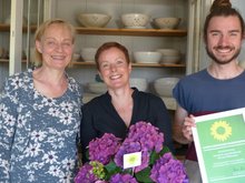 In der Werkstatt der Grünen Gründerin, der Keramikerin Nicole Willmann, findet die Auszeichnung zur Grünen Gründerin statt. Sie lächelt in der Mitte in die Kamera, umrahmt von Petra Budke, der Landesvorsitzenden von Bündnis 90/Die Grünen und Martin Wandrey, ein 24jähriger junger Mann mit Dutt, der für die grüne Partei als Direktkandidat im Havelland, Ostprignitz-Ruppin und der Prignitz antreten wird. Er kommt gebürtig aus Friesack.