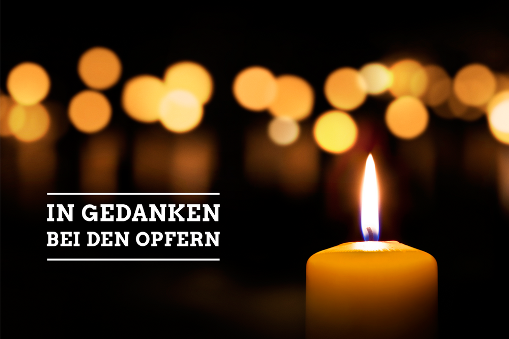 Brennende Kerzen, verwischt, eine leuchtend im Vordergrund. Dazu die Aufschrift: In Gedanken bei den Opfern.