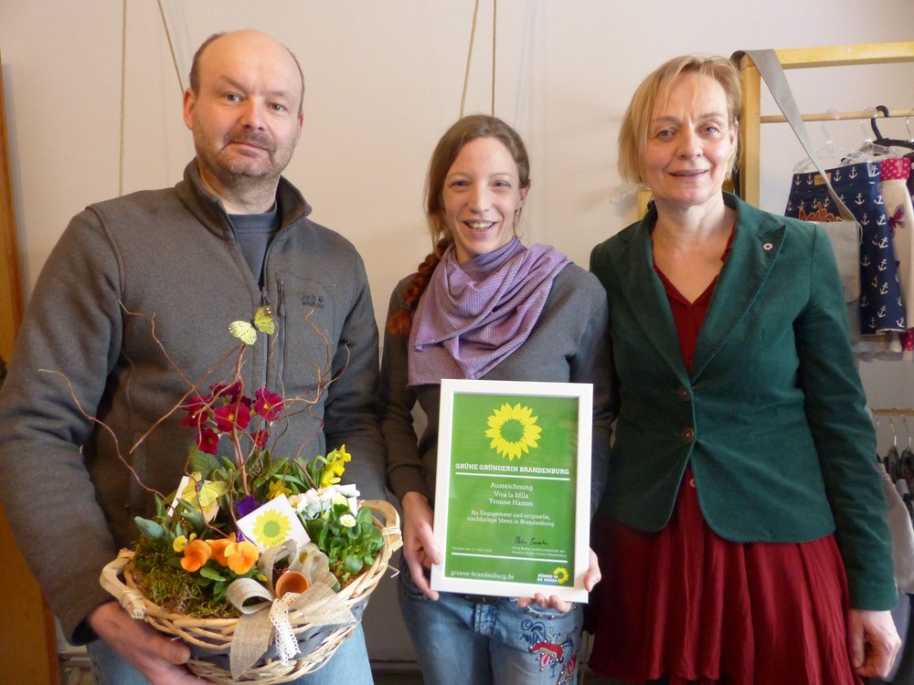 Die neue Grüne Gründerin steht lächelnd und schmal in der Mitte: die 30jährige Yvonne Hamm, die seit zweieinhalb Jahren in Calau lebt. Sie wird vom kreisvorsitzenden aus OSL Stefan Schön und der Landesvorsitzenden Petra Budke in ihrem Atelier umrahmt - samt Blumentopf mit Frühlingsblühern und der Urkunde "Grüne Gründerin".