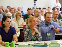 Auf dem Parteitag in Eberswalde vom April 2018 sitzen mit wachsamen Blick und zuversichtlich lächelnd die beiden Landesvorsitzenden Petra Budke und Clemens Rostock in dem holzvertäfelten Raum. Links im Bild neben ihnen ist Annalena Baerbock im nachblauen Kleid, die drei Monate zuvor auf der Bundesdelegiertenkonferenz zur Bundesvorsitzenden gekürt wurde.