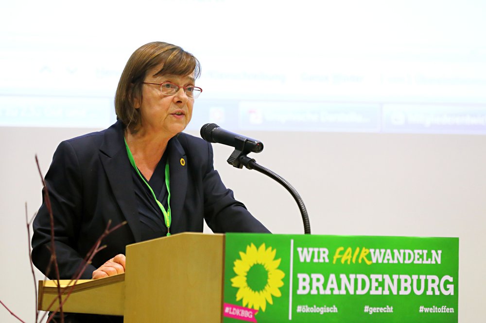 Ursula Nonnemacher spricht auf dem Landesparteitag in Wildau im November 2018 zum Parteiprogramm. Sie hat einen dunklen Blazer an und steht am Rednerpult, das mit dem bündnisgrünen Logo geschmückt ist.